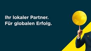 Ein Mann in einem dunklen Anzug mit einem Commerzbank-Anstecker am Revers balanciert eine goldene Weltkugel auf seiner Fingerspitze.