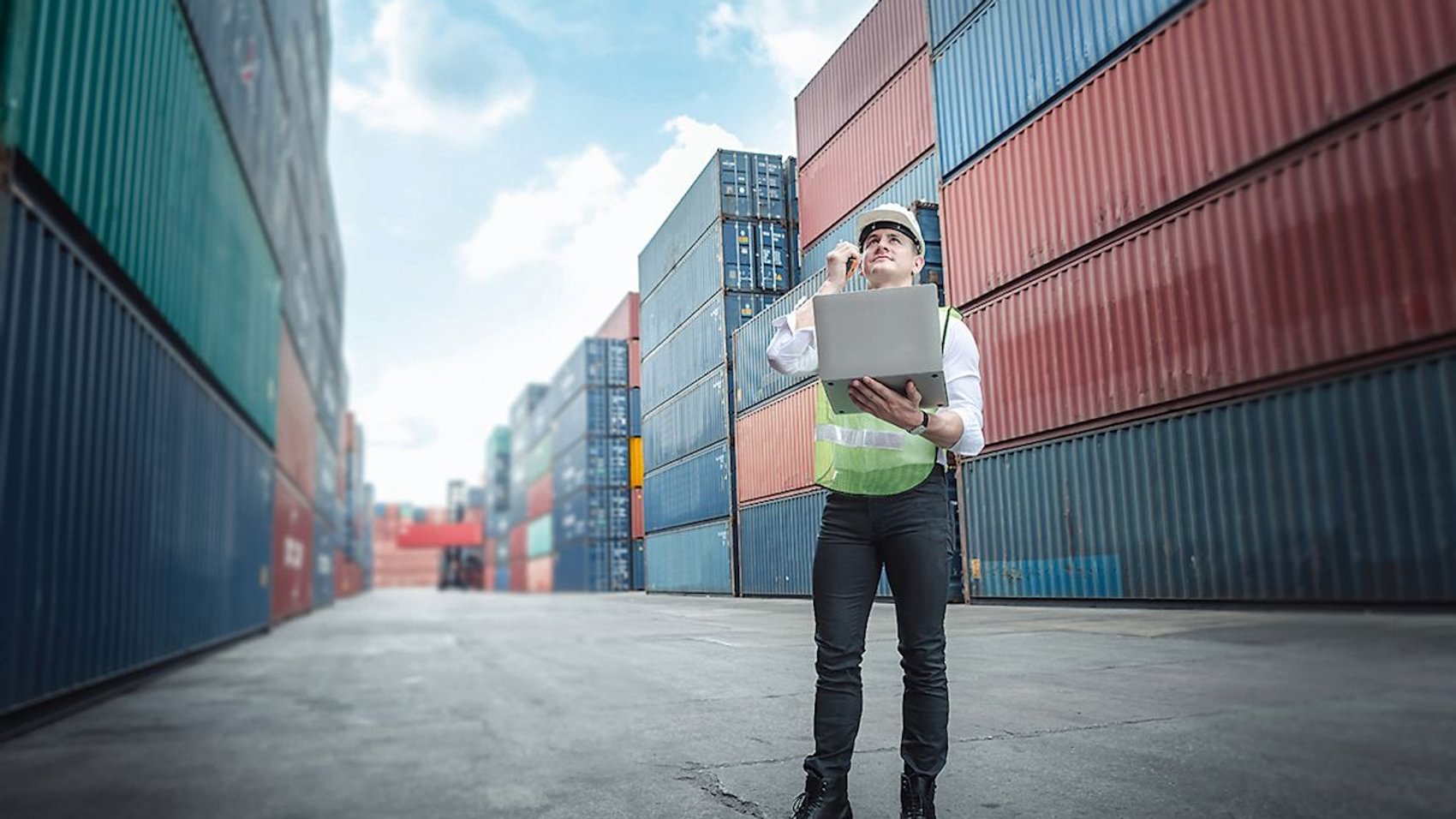 Ein Transportingenieur, der über ein Laptop in einer Containerwerft die Kontrolle der Containerplatzierung verwaltet. 