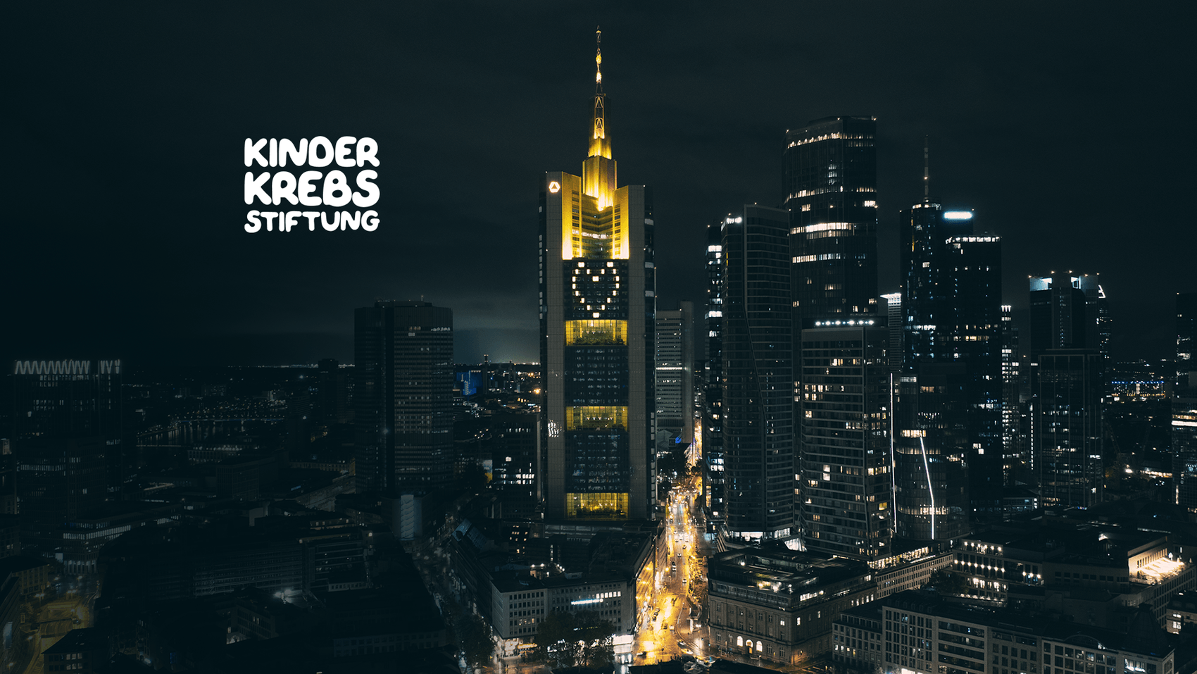 Luftbildaufnahme der Frankfurter Skyline bei Abenddämmerung. Im Vordergrund der beleuchtete Commerzbank Tower, dessen Fassade das leuchtende Commerzbank-Herz zeigt.